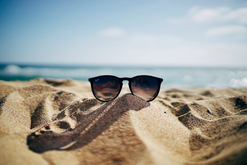 glasses on sand overviewing sea 