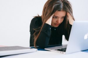 when to fire a client: woman putting hands on head, stressed in front of laptop